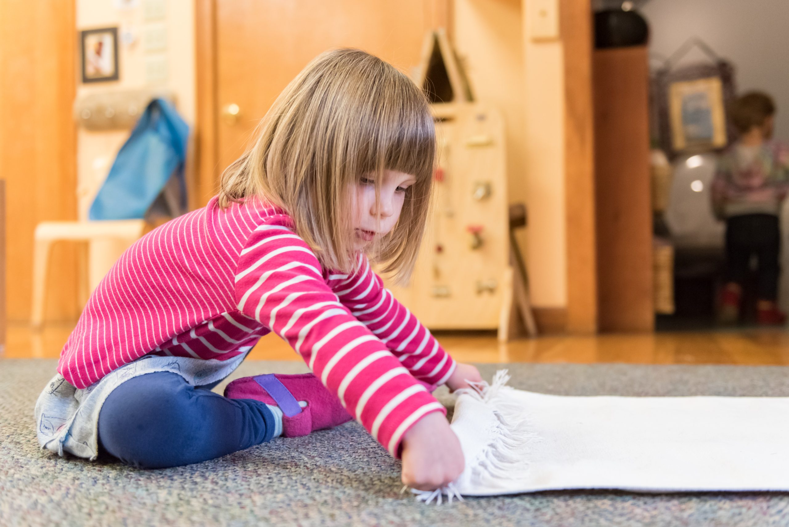 A Montessori toddler student rolls up their sitting blanket