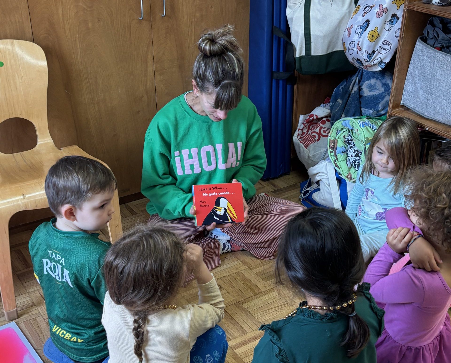 A Montessori Spanish teacher reads a book to Children's House students
